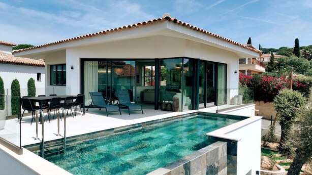 Une maison moderne dotée d’une piscine, d’un espace salon extérieur et d’un patio entièrement vitré.