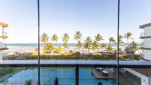 A poolside view with a beach and palm trees in the background. - Modern Apartments by the Beach in Ilheus - PET (Ilhéus)