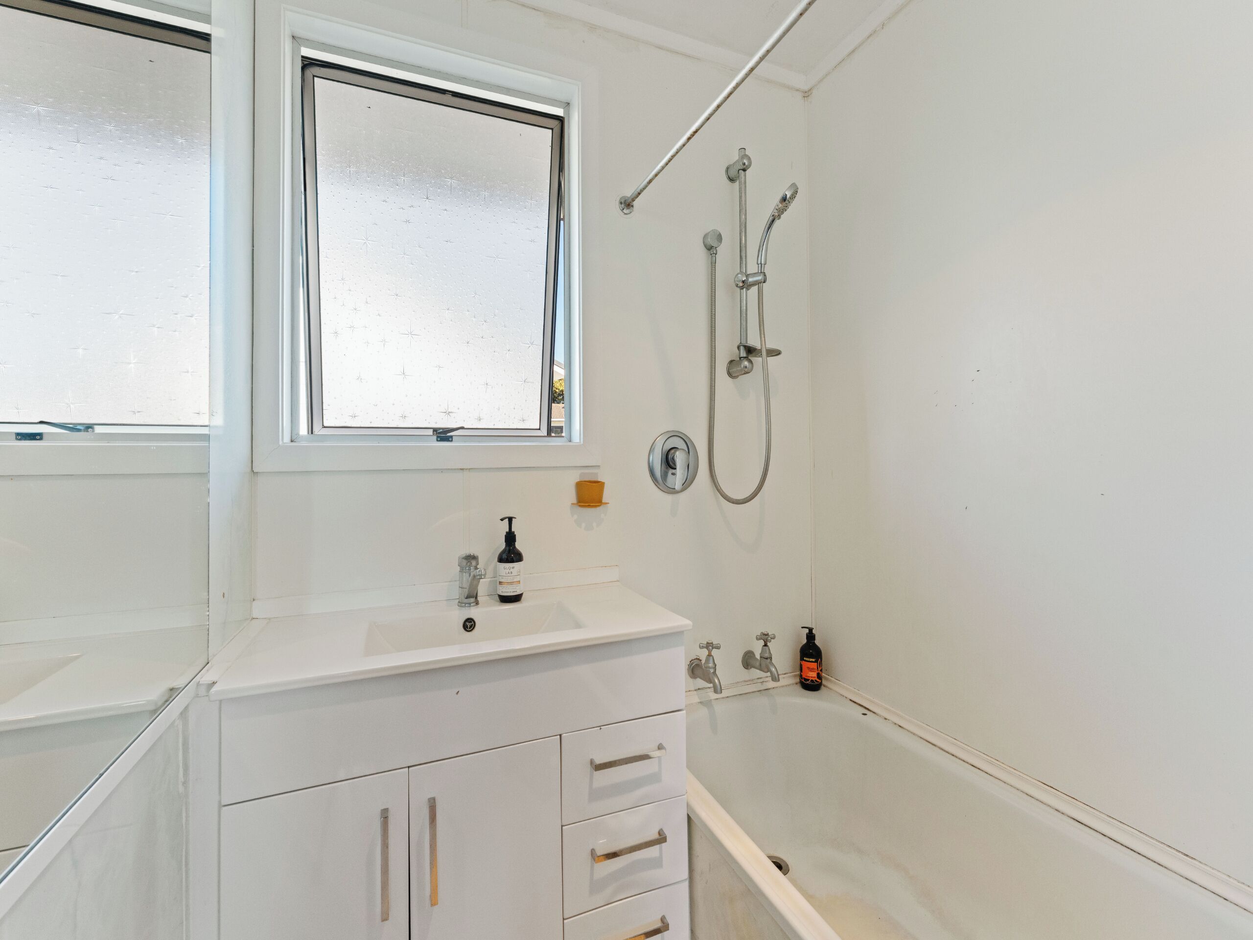 Une salle de bain avec un lavabo blanc, une fenêtre, une douche et des toilettes.