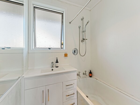 A bathroom with a white sink, a window, a shower, and a toilet.
