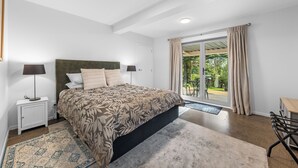 Une chambre moderne avec un grand lit, deux lampes de chevet, une tête de lit verte et une vue sur l’extérieur grâce à une porte-fenêtre coulissante.