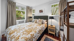 Une chambre à coucher avec un grand lit, une table de chevet, une lampe, une bibliothèque et une fenêtre avec des rideaux.