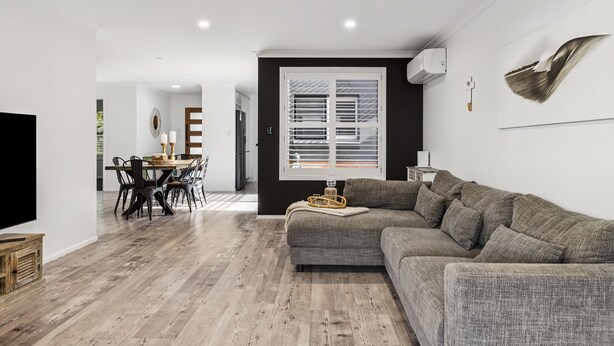 A modern living room with a sectional sofa, a dining area with a table and chairs, and a large window with blinds. - Beachside 24 - Pet Friendly Holiday Home - Holiday Yamba (Yamba)