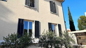 Un edificio de dos pisos con tres ventanas, cada una con contraventanas, y un balcón.