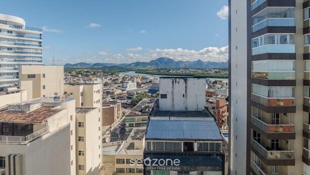 Un immeuble de grande hauteur doté de nombreux balcons, offrant une vue dégagée sur le paysage urbain et les montagnes au loin, et comportant un filigrane avec le texte « sedzone ».