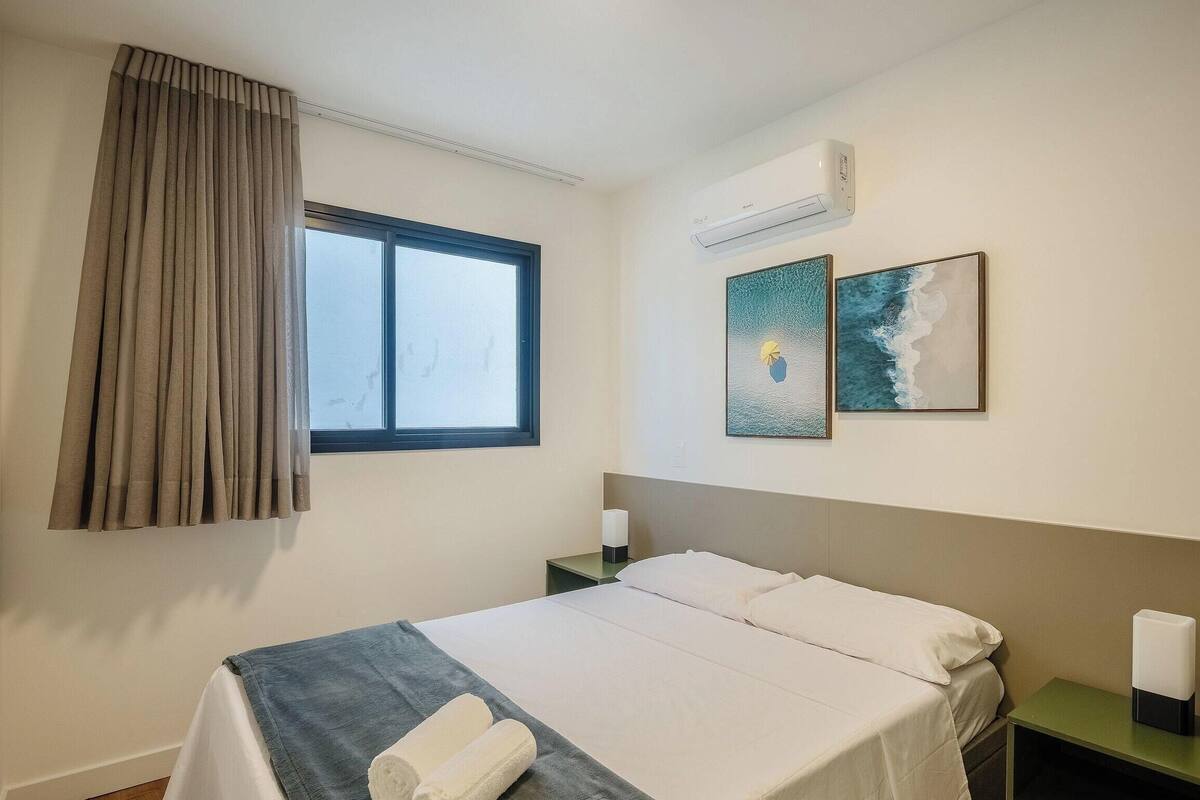 Ein Hotelzimmer mit einem Bett, einem Vorhangfenster, einer Klimaanlage und zwei Wandbildern.
