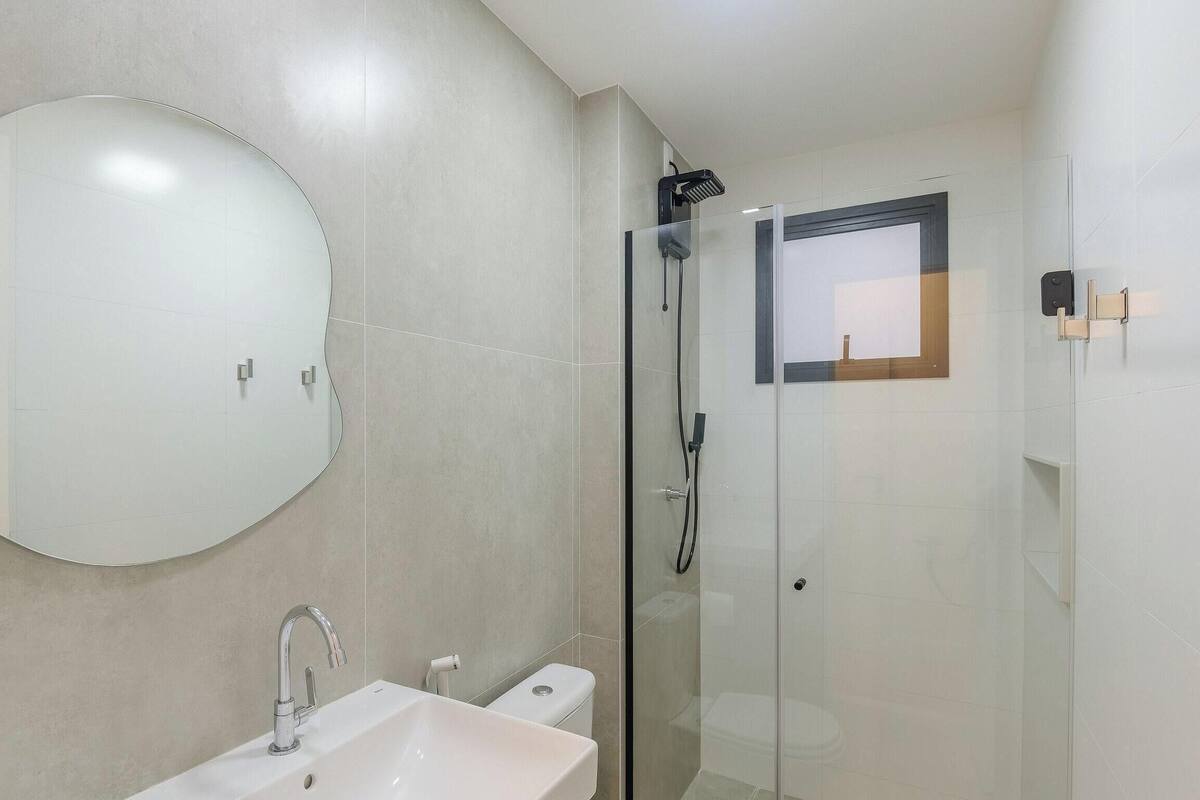 Ein Badezimmer mit rundem Spiegel, Waschbecken, Toilette und einer Duschkabine.