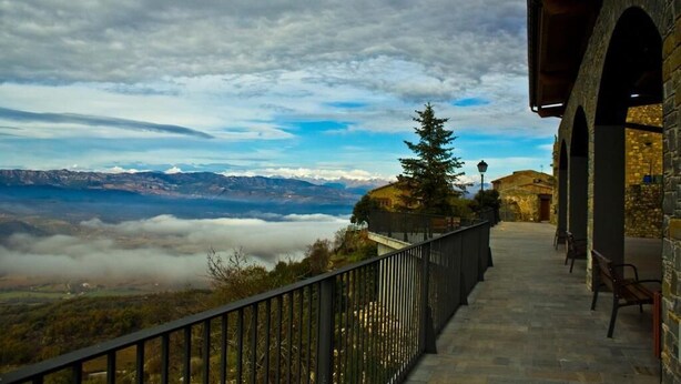 A stone pathway leading to a balcony with a view of mountains and clouds.