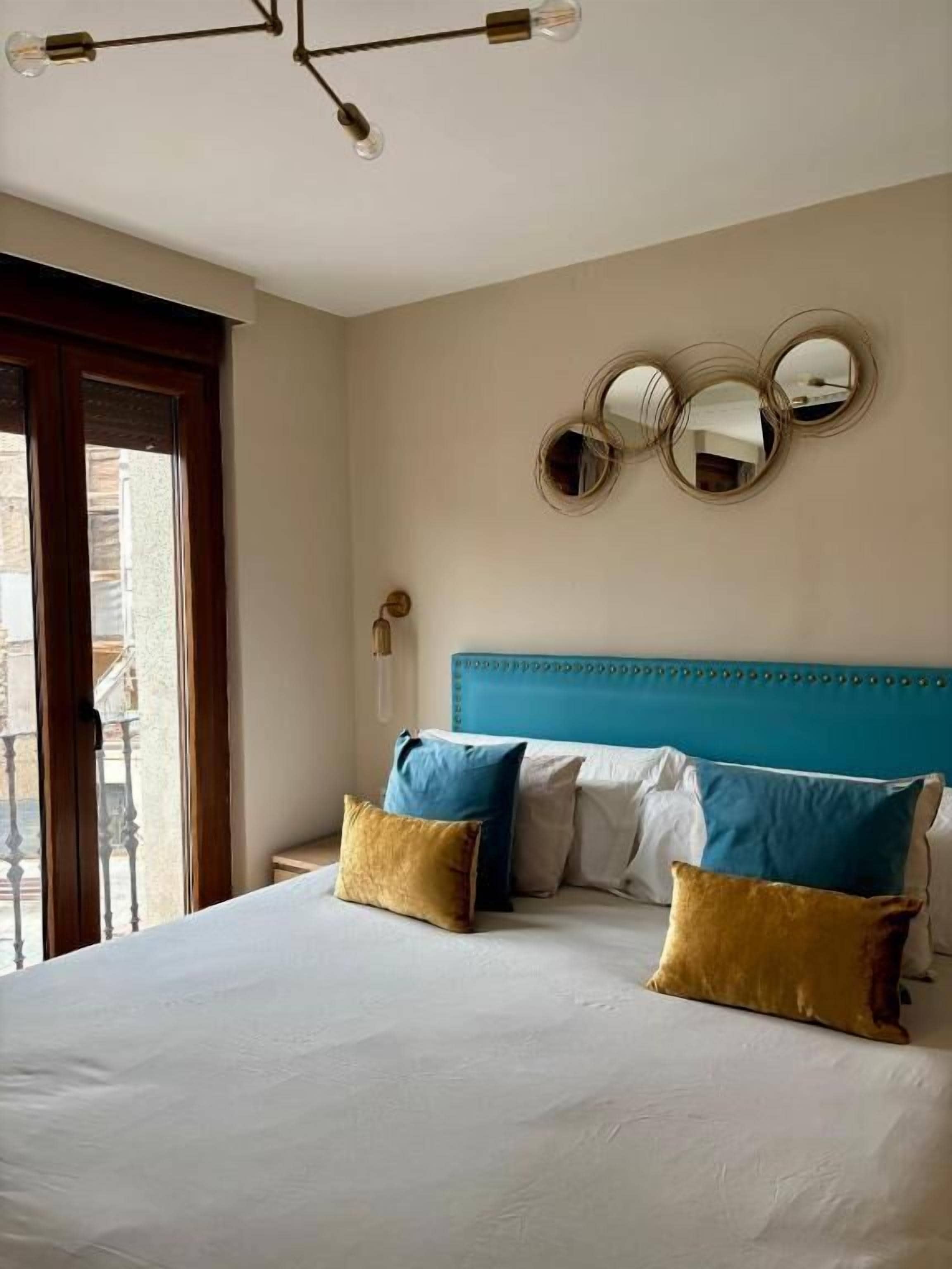 A hotel room with a bed, a blue headboard, and three round mirrors on the wall.