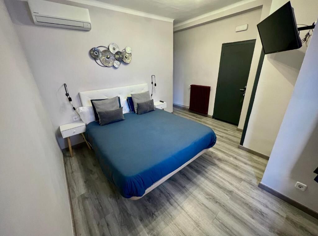 Um quarto com cama, mesas de cabeceira, relógio de parede e televisão de tela plana fixada na parede.