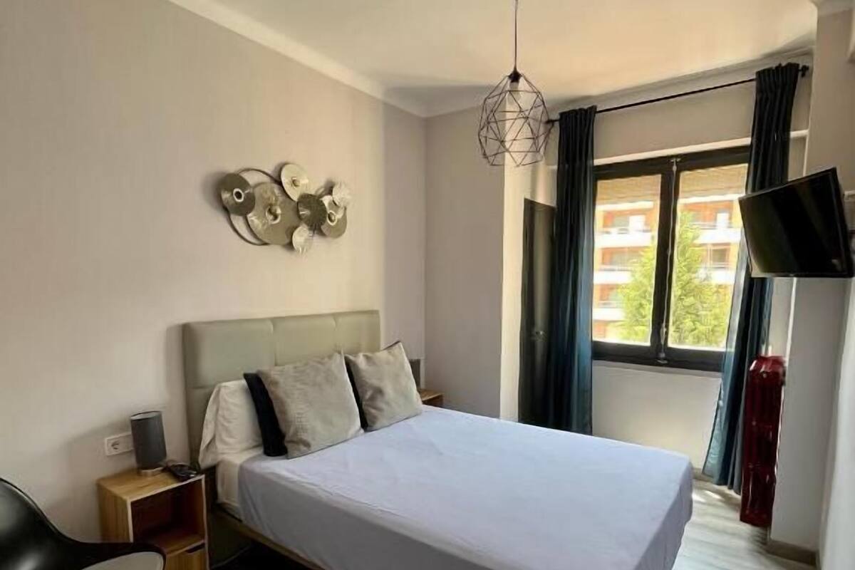 Une chambre d’hôtel moderne équipée d’un lit, d’un bureau, d’une chaise, d’un téléviseur à écran plat et d’une fenêtre avec des rideaux.