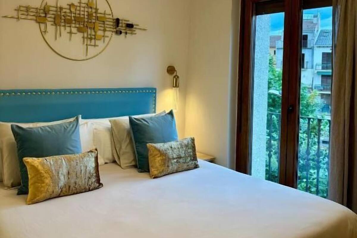 Une chambre d’hôtel avec un grand lit, une tête de lit bleue et une vue sur l’extérieur par une fenêtre.
