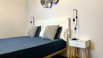 Quarto bem arrumado com cama, mesa de cabeceira e arte decorativa na parede.