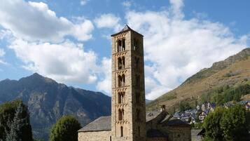 Une église en pierre dotée d’un clocher, entourée de montagnes et d’un petit village.