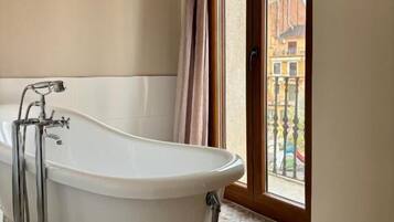Un baño con una bañera independiente, un ventanal con vista a edificios y baldosas de suelo con diseños.