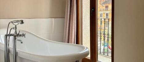 A bathroom with a freestanding bathtub, a window with a view of buildings, and patterned floor tiles.