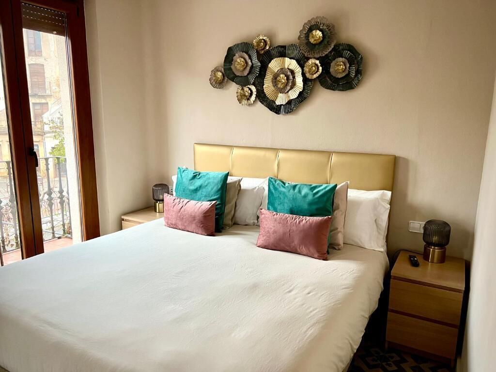 A hotel room with a large bed, two nightstands, a decorative wall piece, and a view through a window.