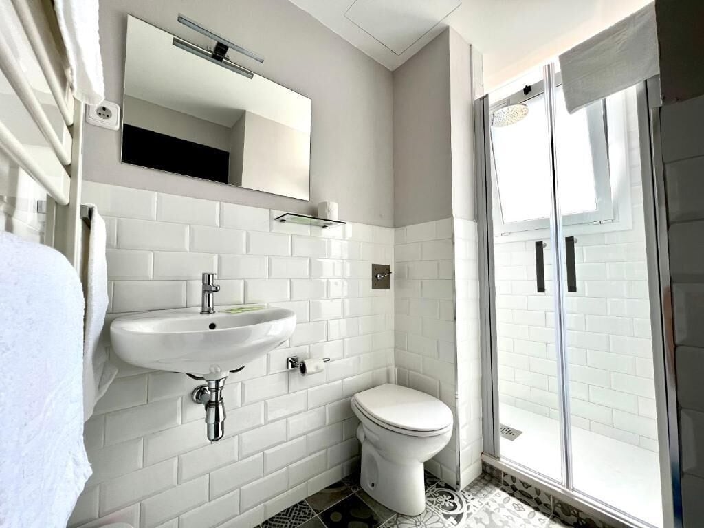 A modern bathroom with white subway tiles, a white sink, a toilet, and a glass shower enclosure.