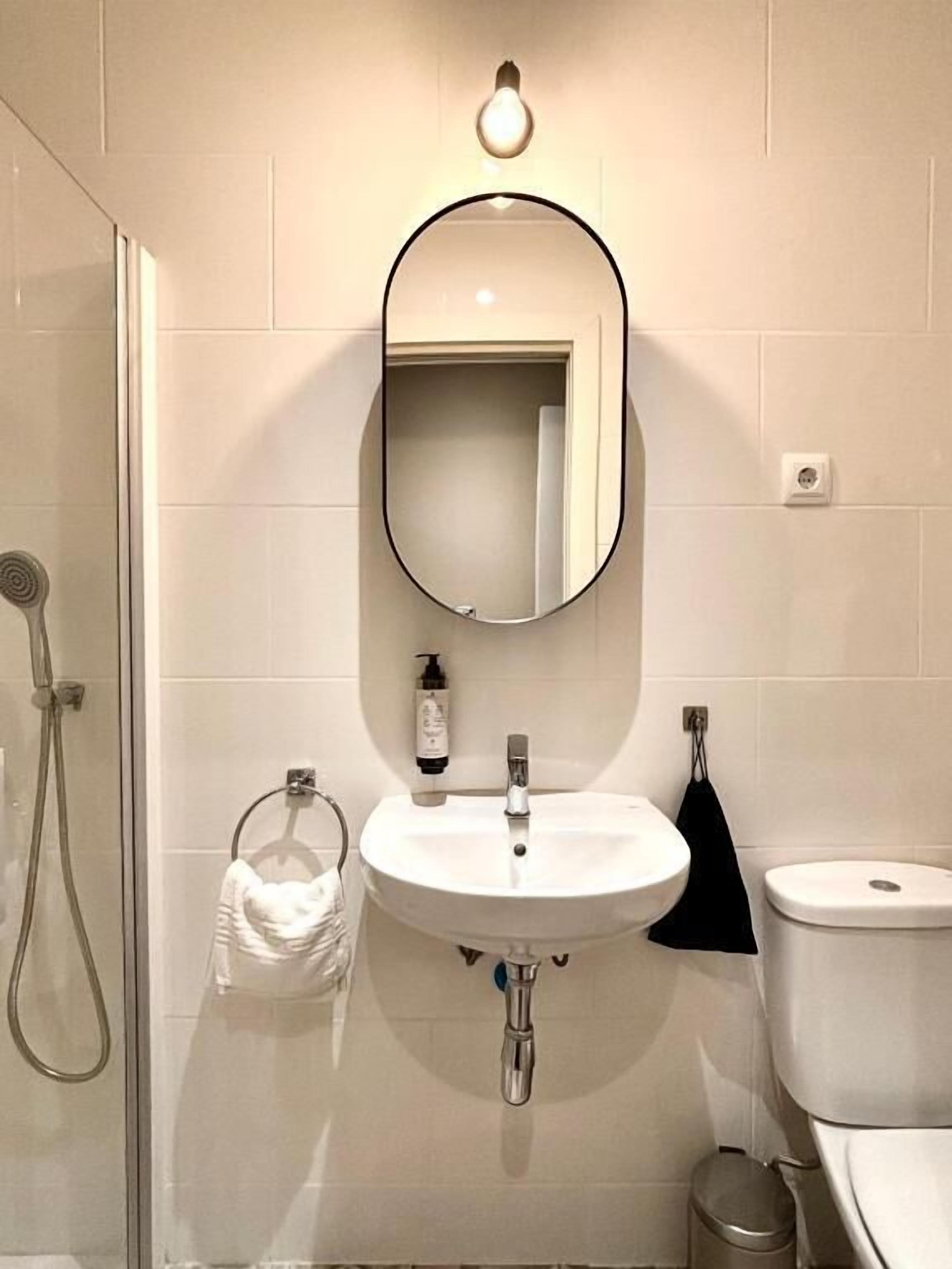 Une salle de bain avec un miroir rond, un lavabo blanc et des toilettes.