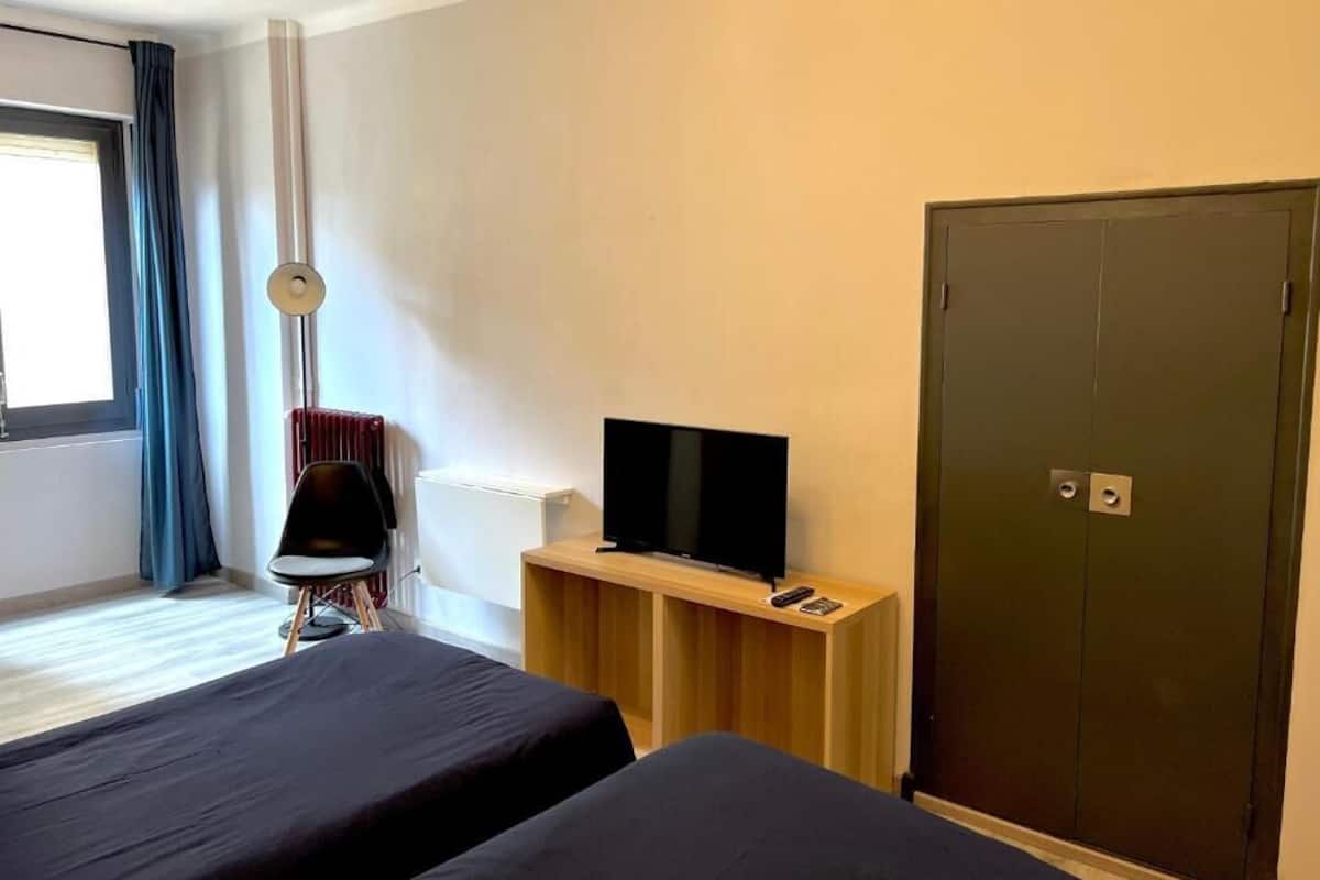 Une chambre d’hôtel avec deux lits, un téléviseur posé sur un meuble en bois, une armoire et une chaise.