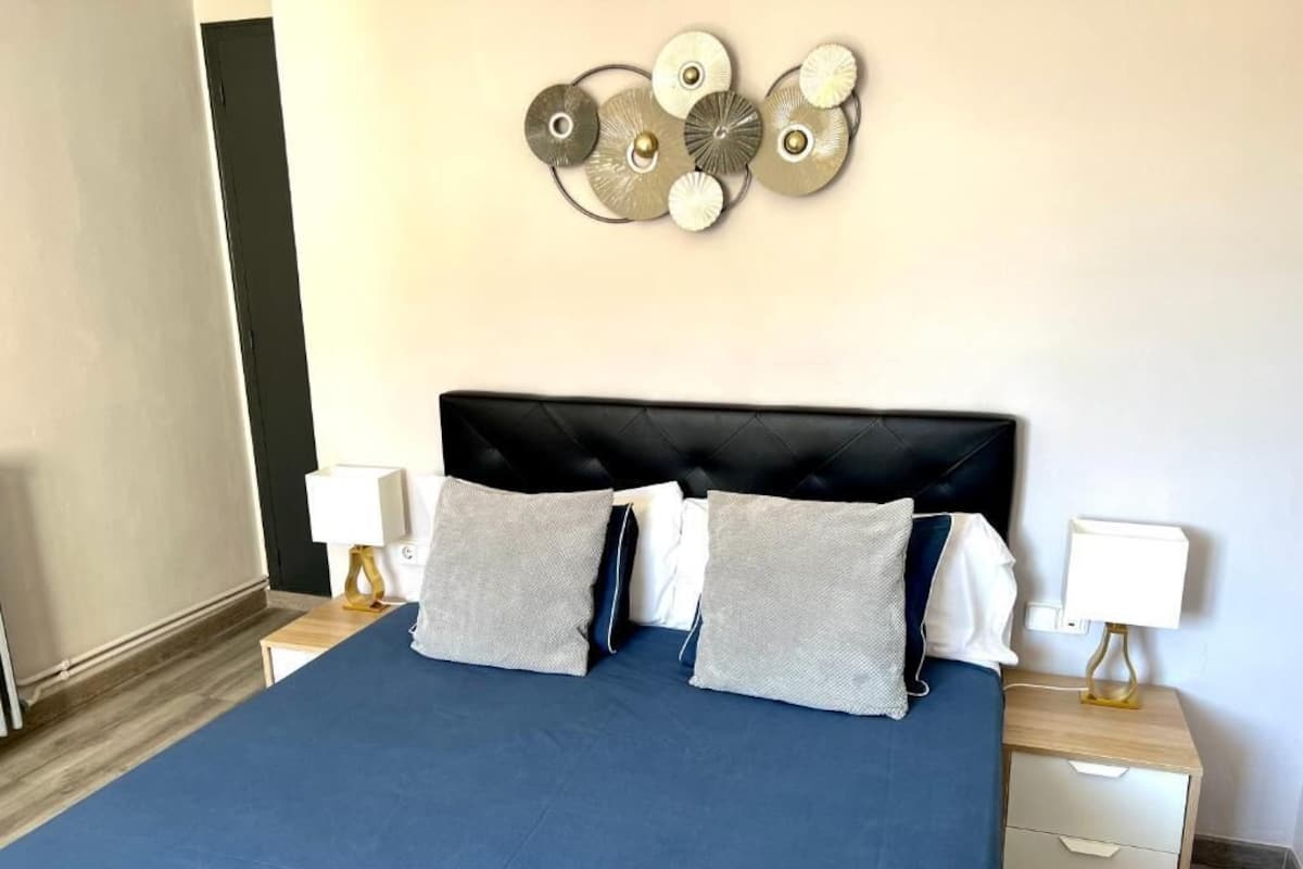 Une chambre avec un grand lit, deux tables de chevet et une œuvre d’art murale au-dessus du lit.