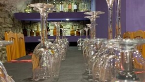 A row of empty wine glasses on a table in a room with stone walls and purple decor.