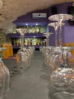 Una hilera de copas de vino vacías sobre una mesa en una habitación con paredes de piedra y decoración morada.