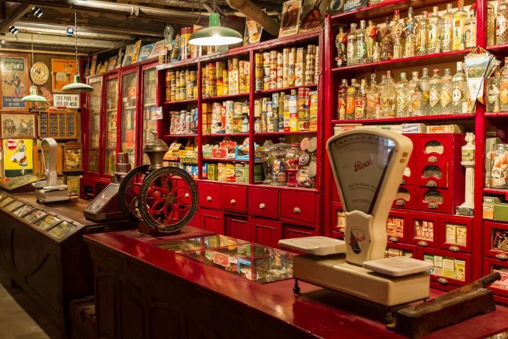 A vintage store with shelves stocked with canned goods and bottles, a weighing scale, and vintage items on display.