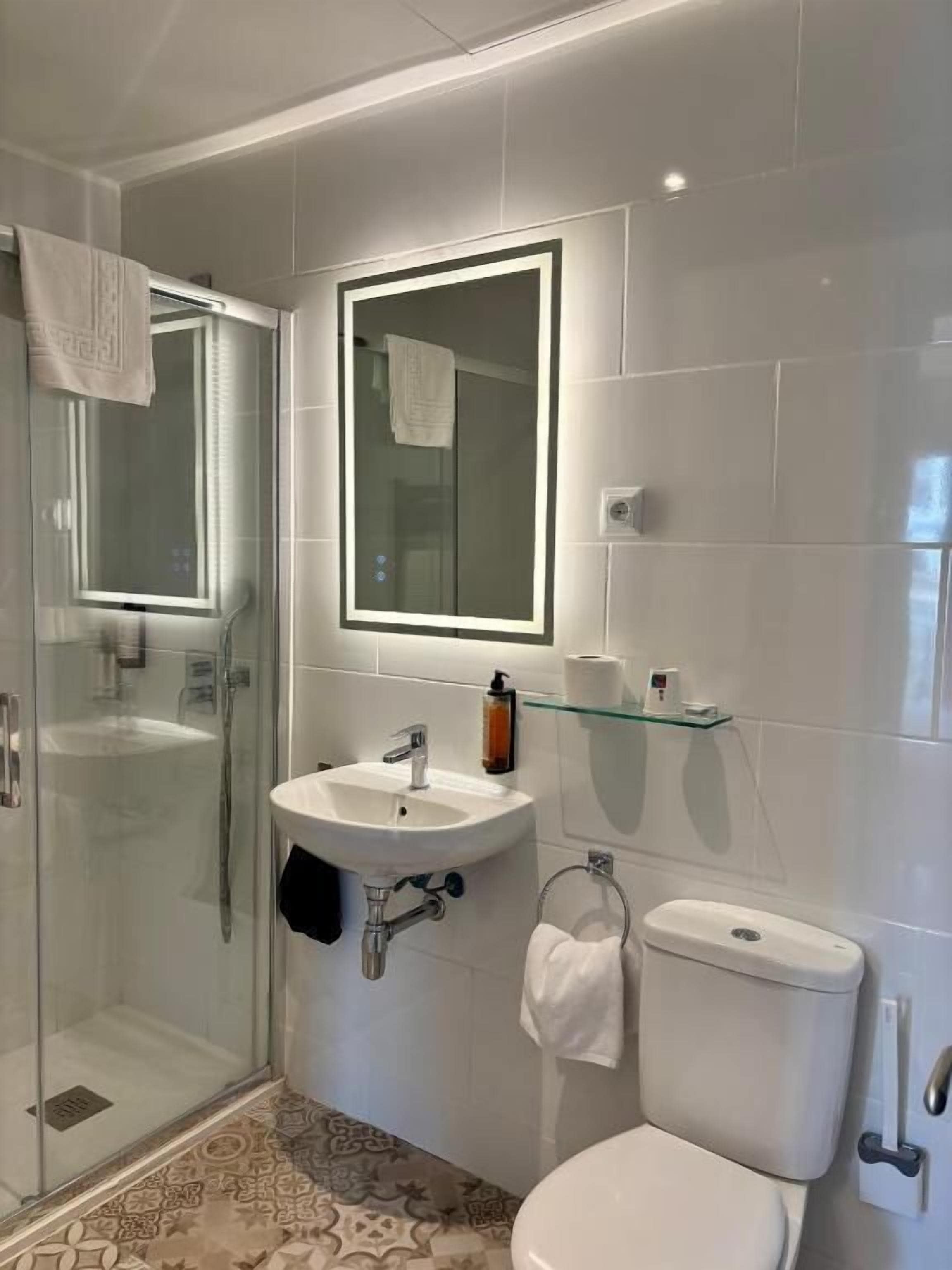 Un baño moderno con ducha de vidrio, un lavamanos blanco con un espejo encima y un inodoro.
