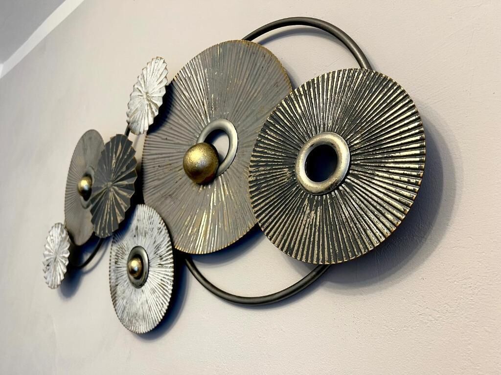 Een wanddecoratie van metaal met cirkelvormige en bladeren-achtige elementen.