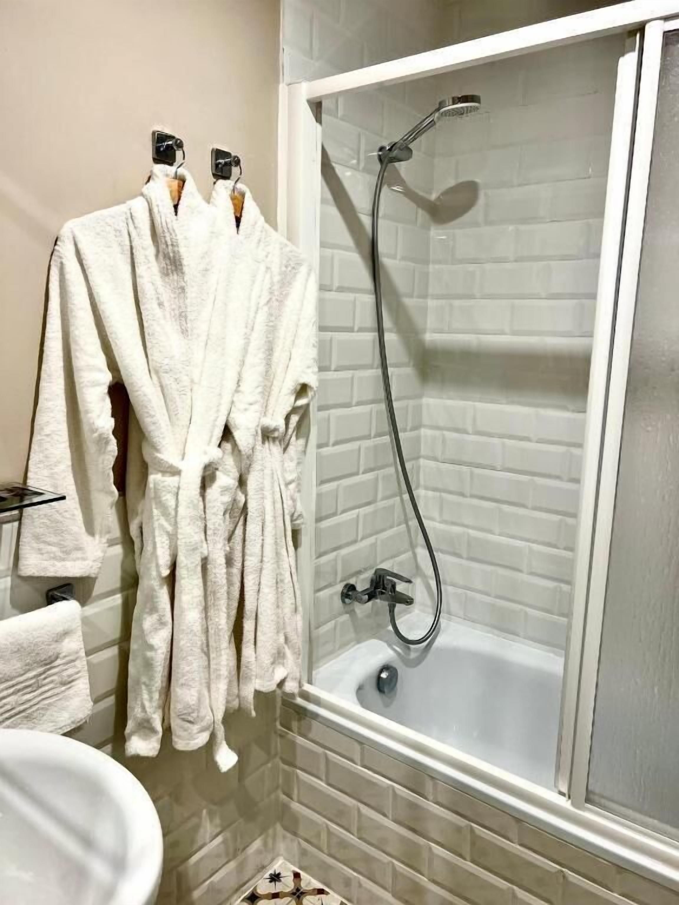 A bathroom with a bathtub, a shower, and two white bathrobes hanging on hooks.
