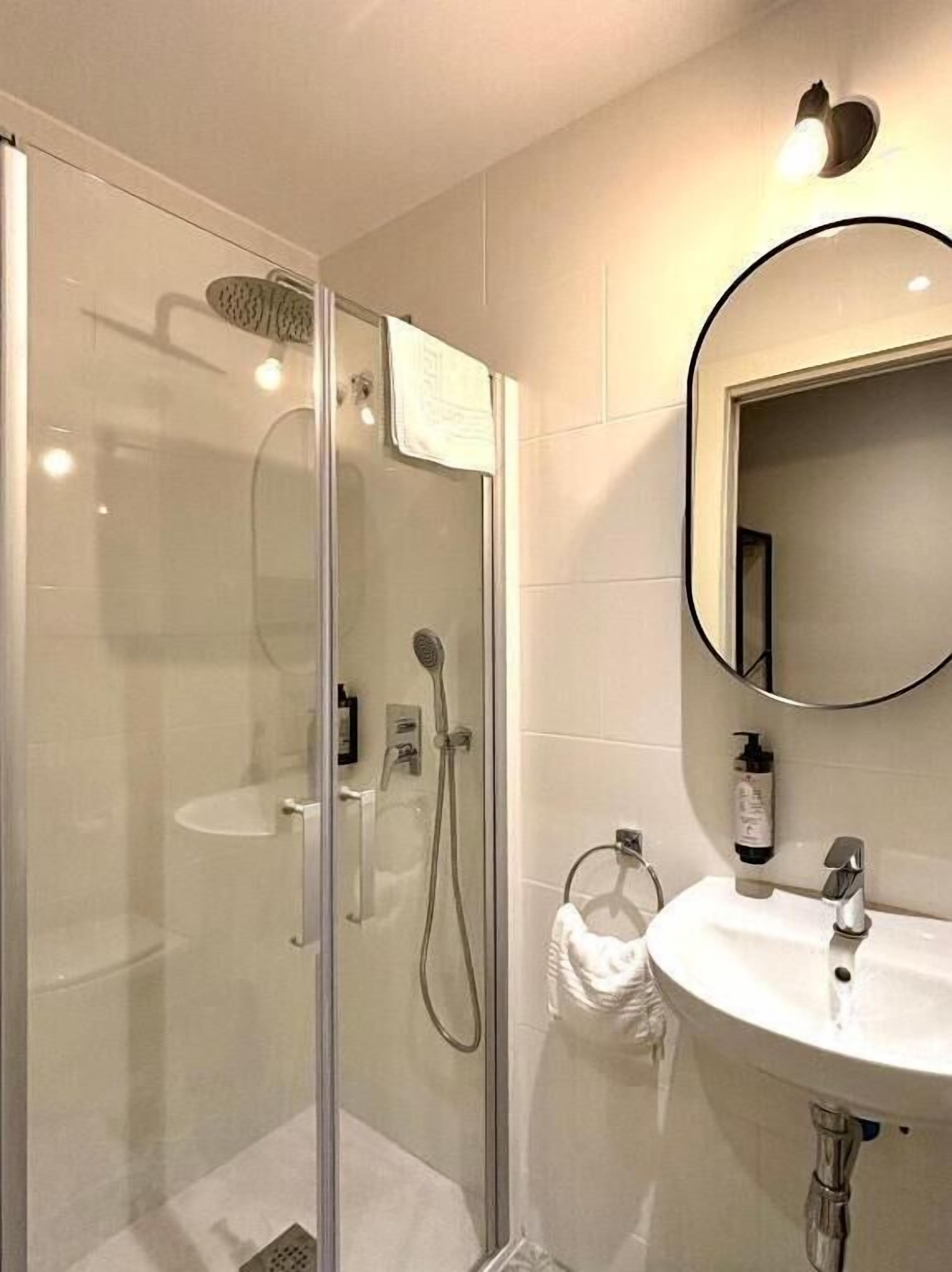 Un baño moderno con ducha acristalada, lavabo blanco y espejo redondo.