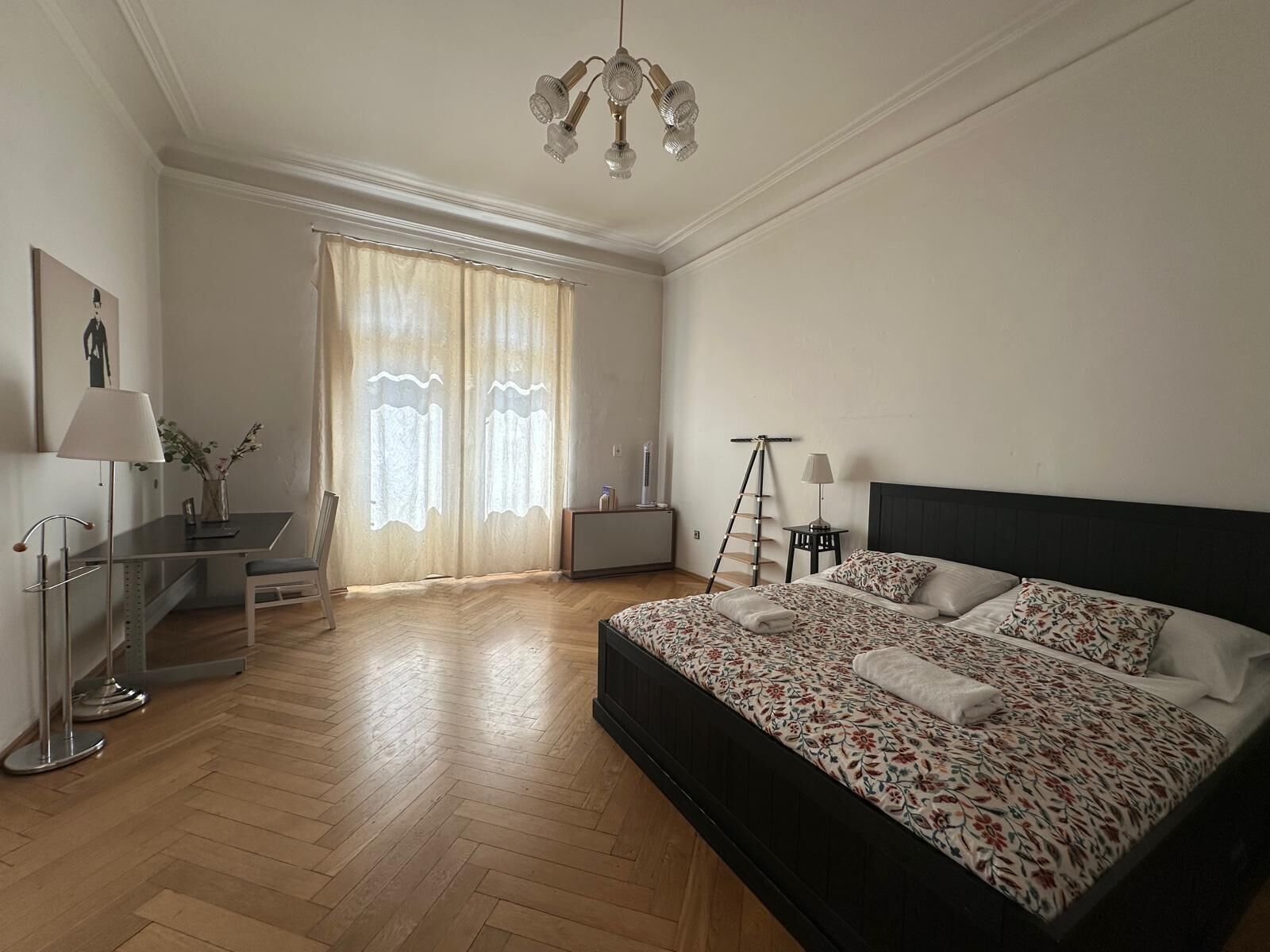Un dormitorio con una cama grande, un escritorio, una silla, una escalera y una ventana con cortinas.