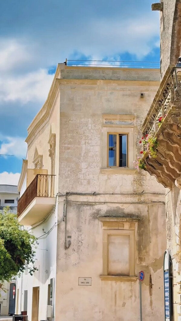 A building with a balcony, a small window, and a door. - PALAZZO VIGILARIUM - Boutique Rooms  (Uggiano la Chiesa)