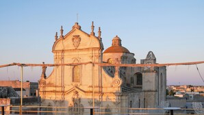 A historic building with ornate architecture, including a large dome and a bell tower, viewed from a terrace with outdoor seating. - PALAZZO VIGILARIUM - Boutique Rooms (Uggiano la Chiesa)