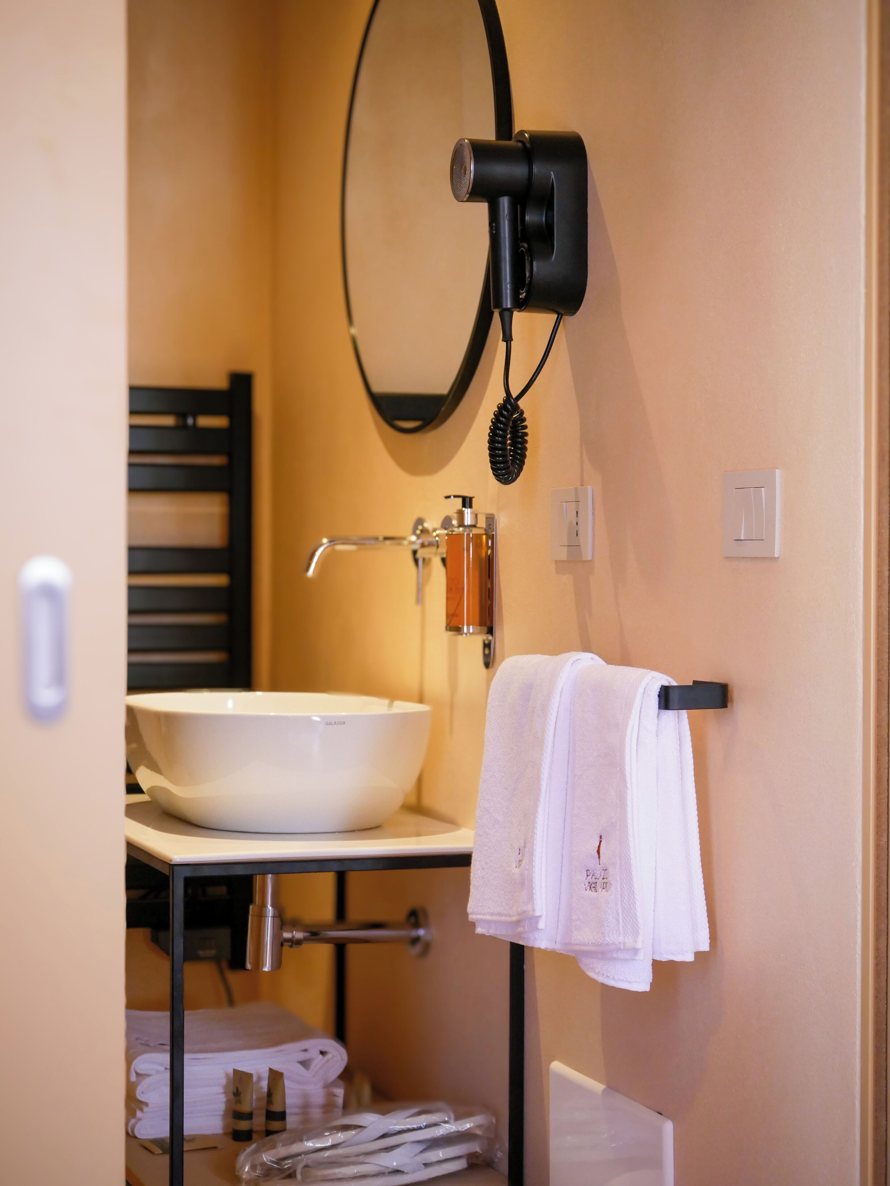 A bathroom with a white sink, a towel rack with a white towel, a hairdryer mounted on the wall, and a mirror.