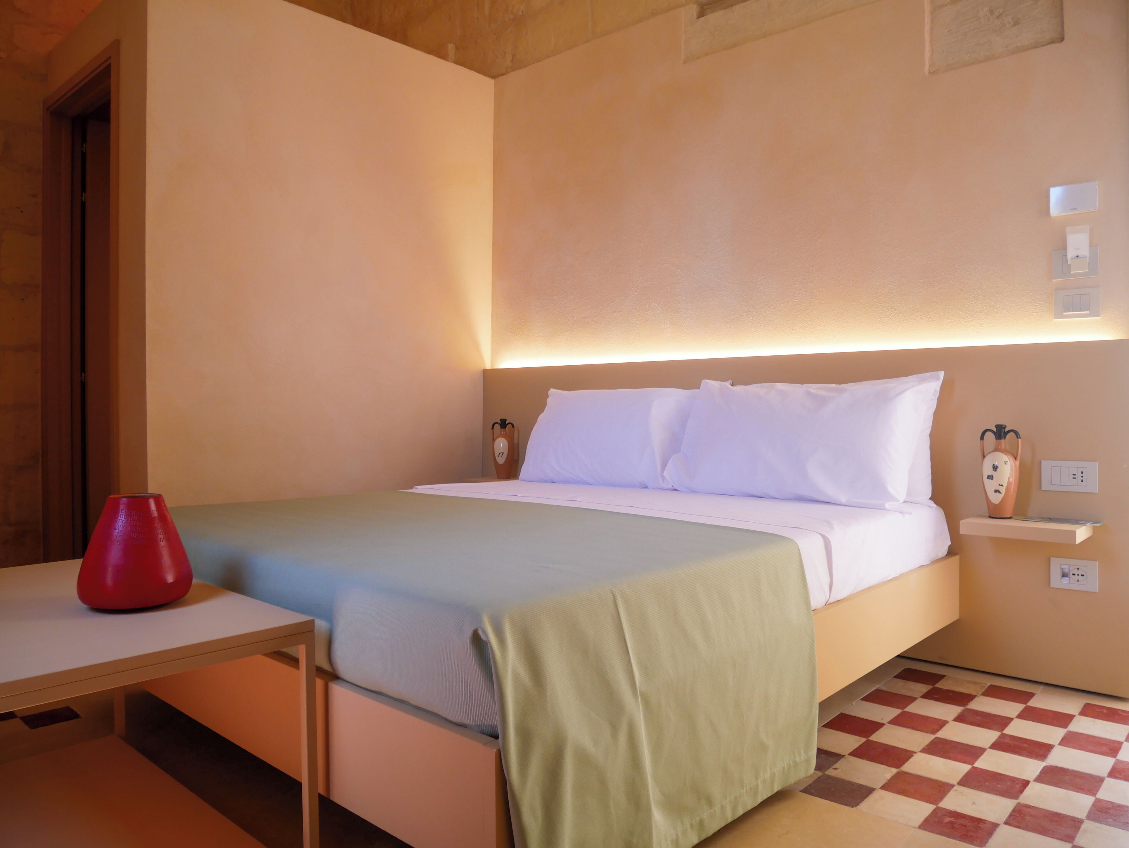 Een hotelkamer met een bed, nachtkastje en een rode vaas.