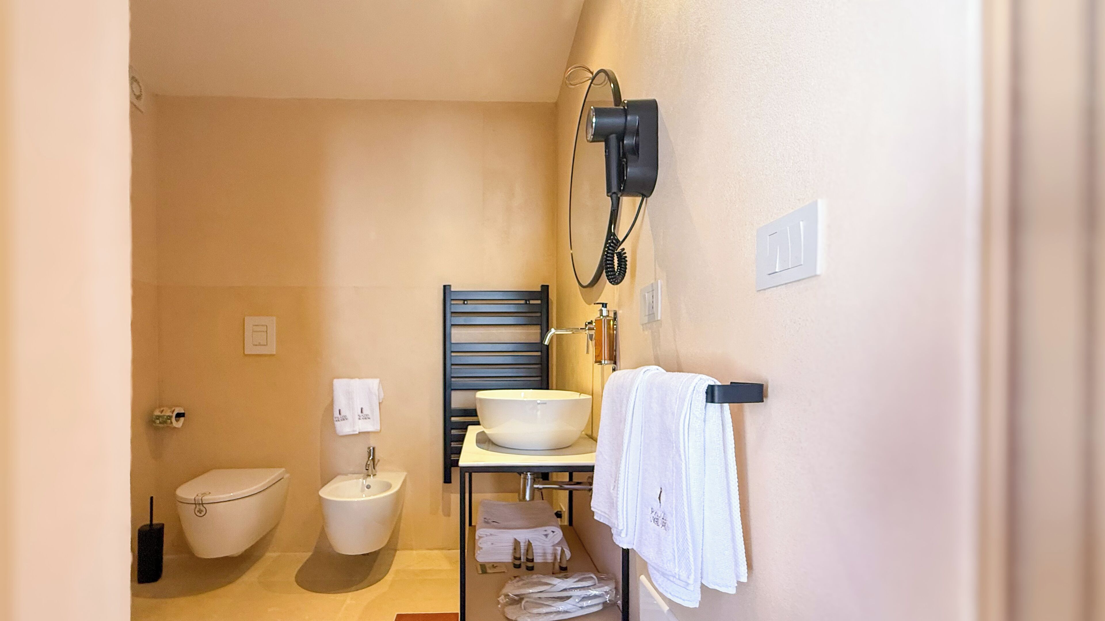 Baño compacto con inodoro, bidé y lavamanos. Hay toallas y artículos de aseo en el mostrador.