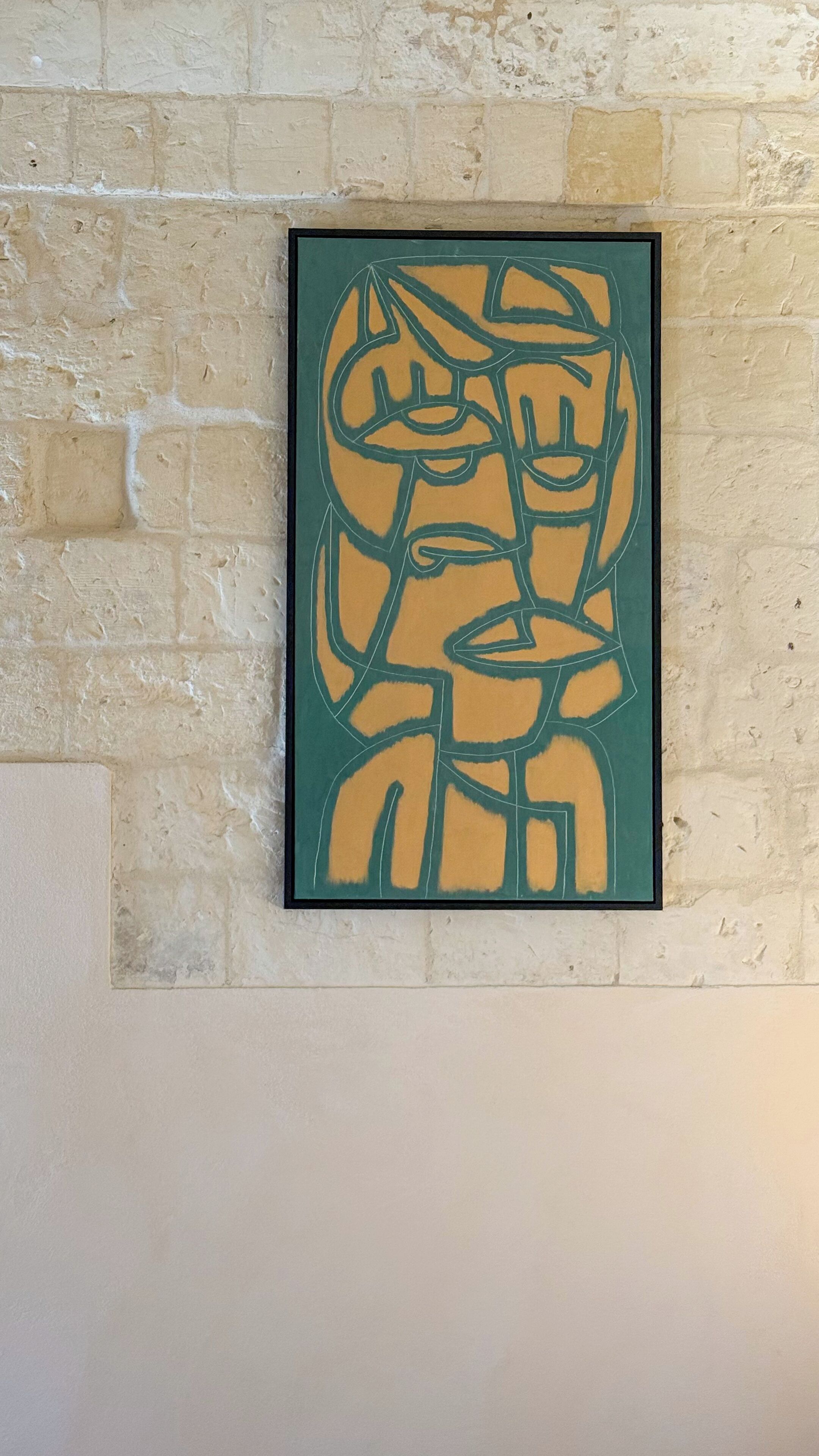 A framed abstract artwork on a brick wall.
