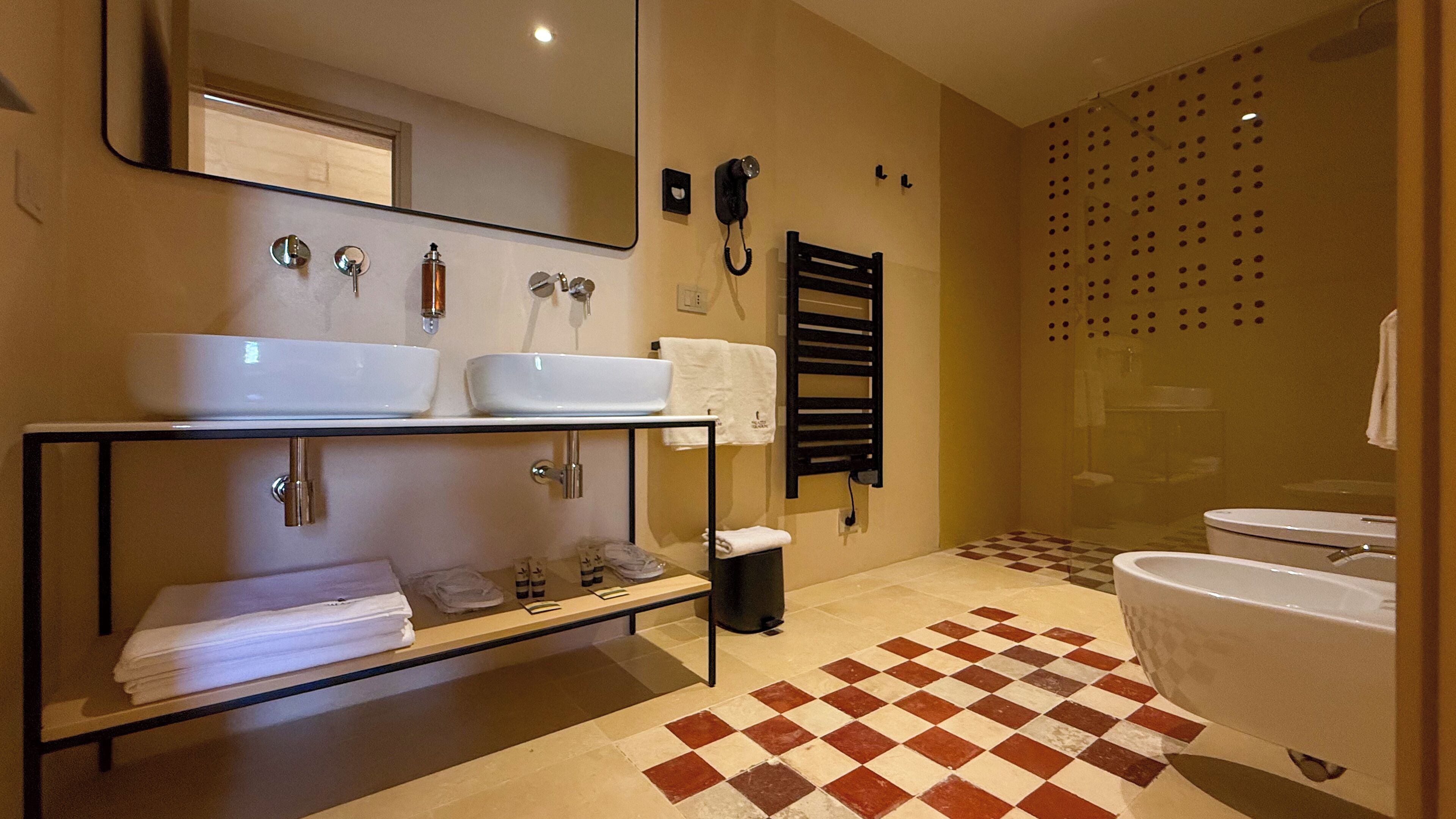 Ein modernes Badezimmer mit zwei Waschbecken, einem großen Spiegel, einer Handtuchheizung, einer Dusche mit Lochblechglasabtrennung und einem Schachbrettboden.