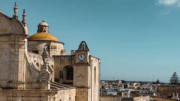 Un edificio histórico con una cúpula destacada y una torre del reloj, visto desde una terraza con suelo de piedra.