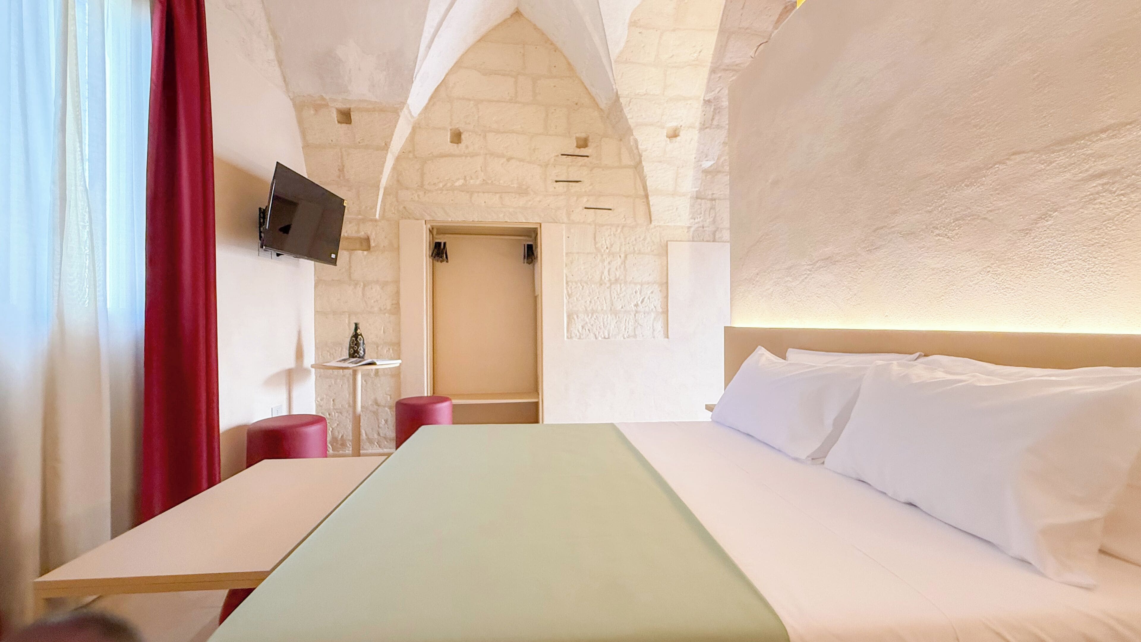 Una habitación de hotel con una cama, una mesa, un televisor y una mesita con un florero.