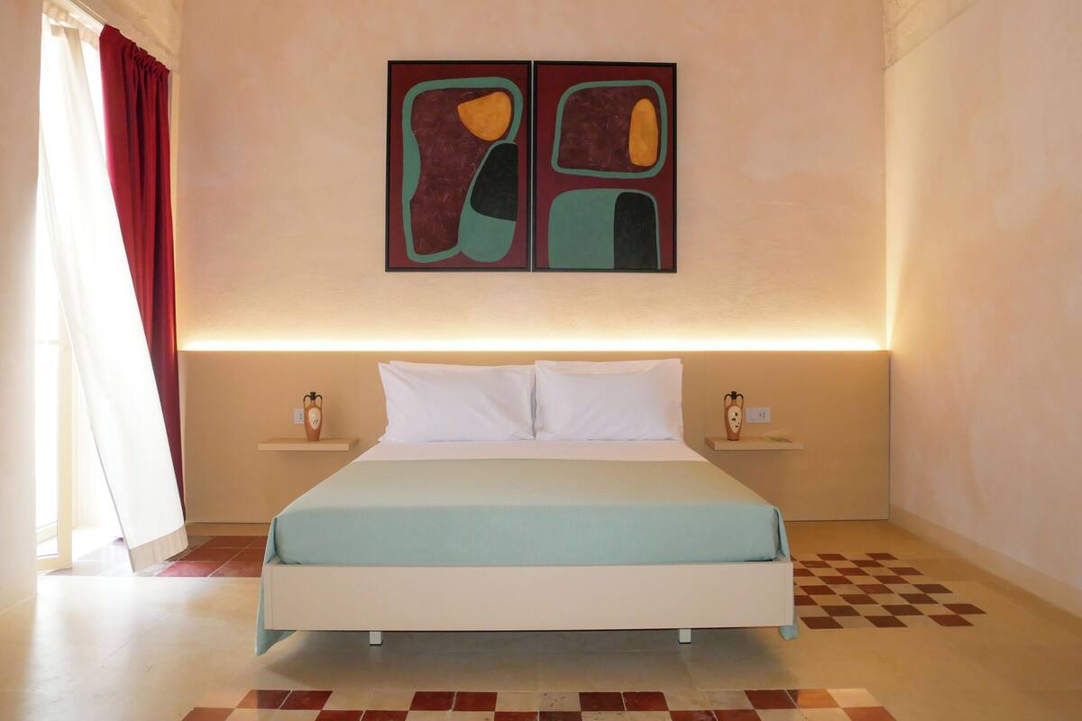 Une chambre d’hôtel comprenant un lit, deux tables de chevet, une œuvre d’art accrochée au mur et un motif à carreaux sur le sol.