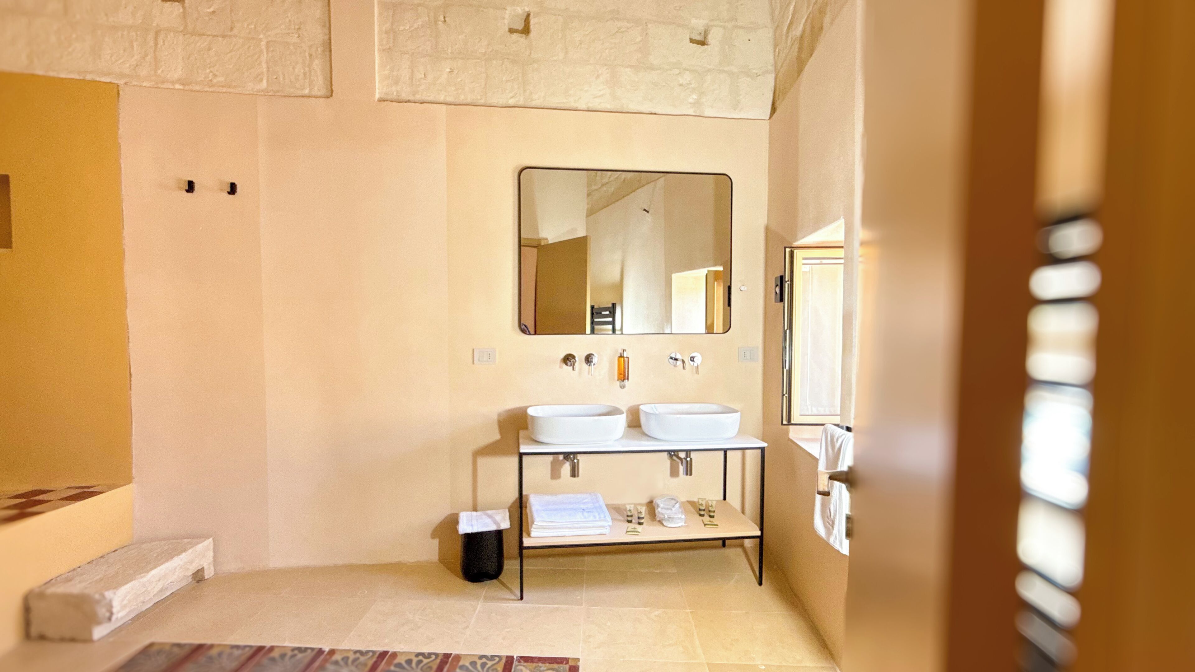 Une salle de bain moderne avec deux lavabos, un grand miroir et une petite poubelle.