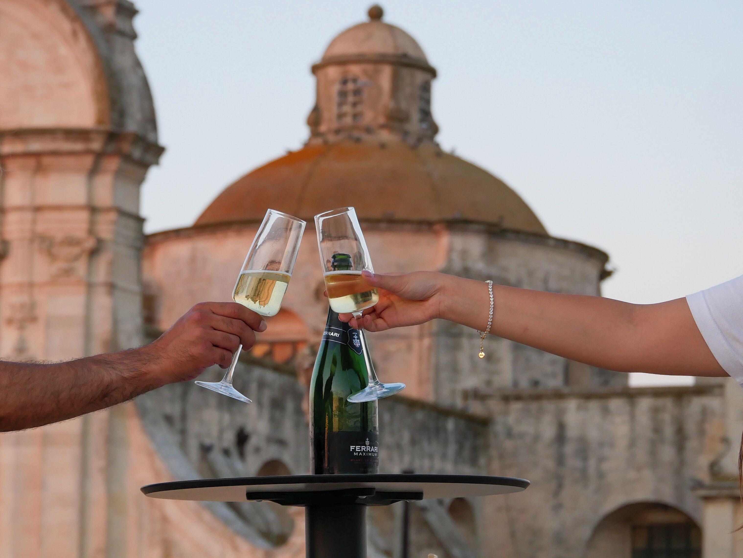 Two people toasting with champagne glasses in front of a historic building with domed architecture.