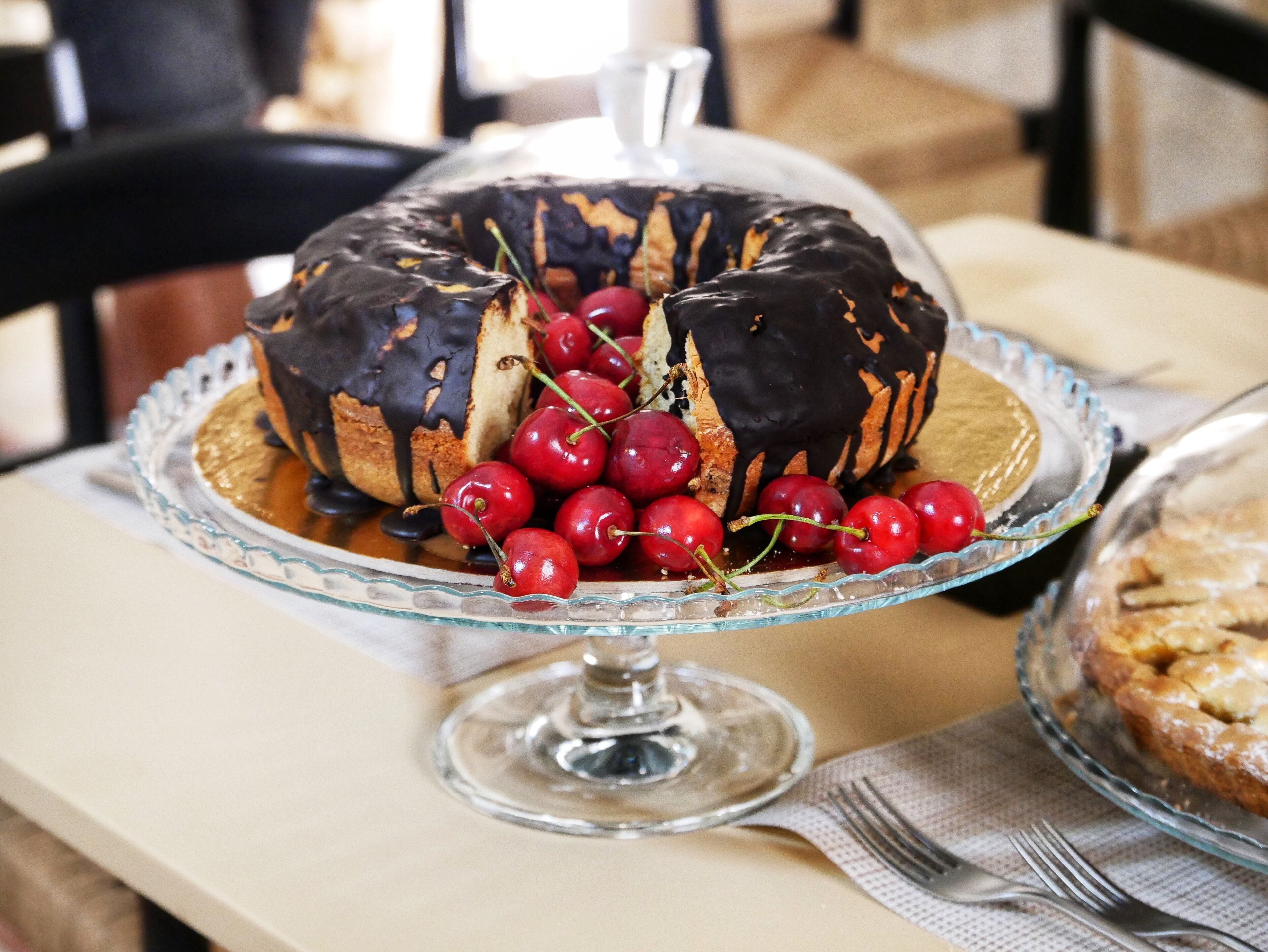 A dessert with chocolate drizzle and cherries on a glass cake stand.