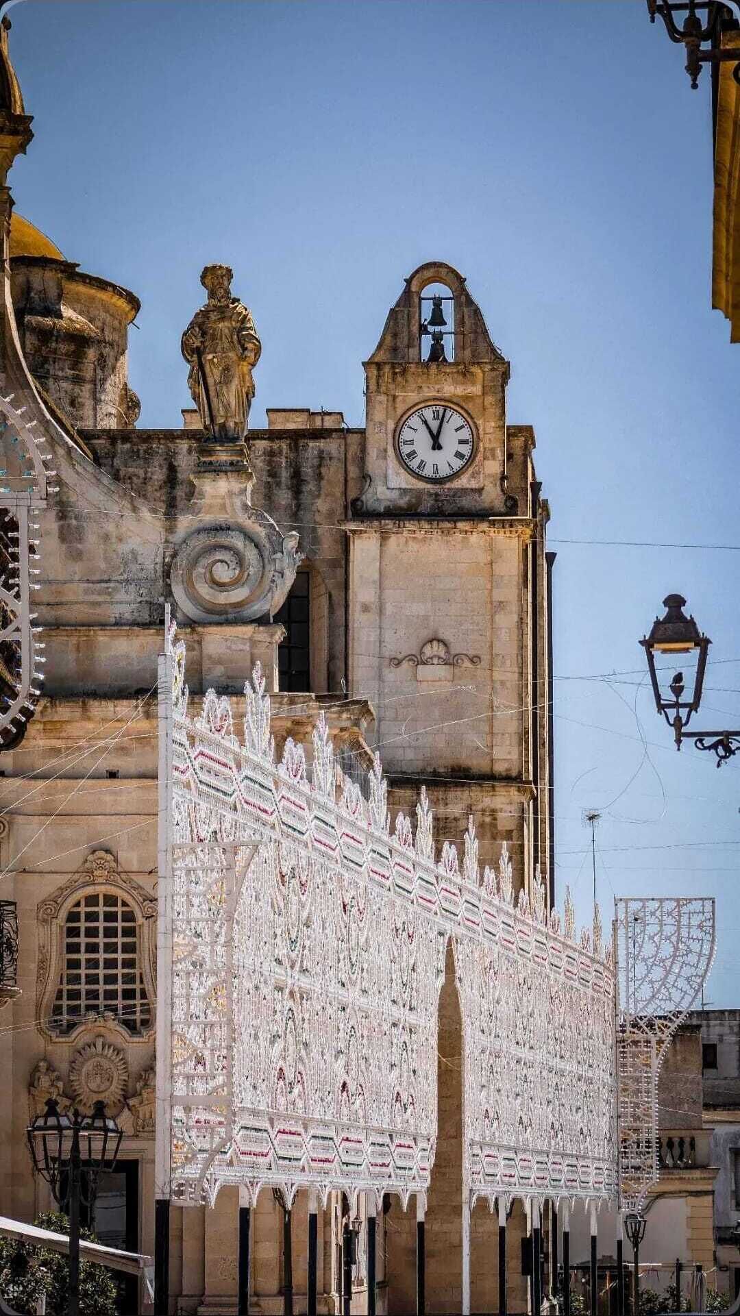 Een historisch gebouw met een klokkentoren, sierlijk ijzerwerk en een standbeeld.