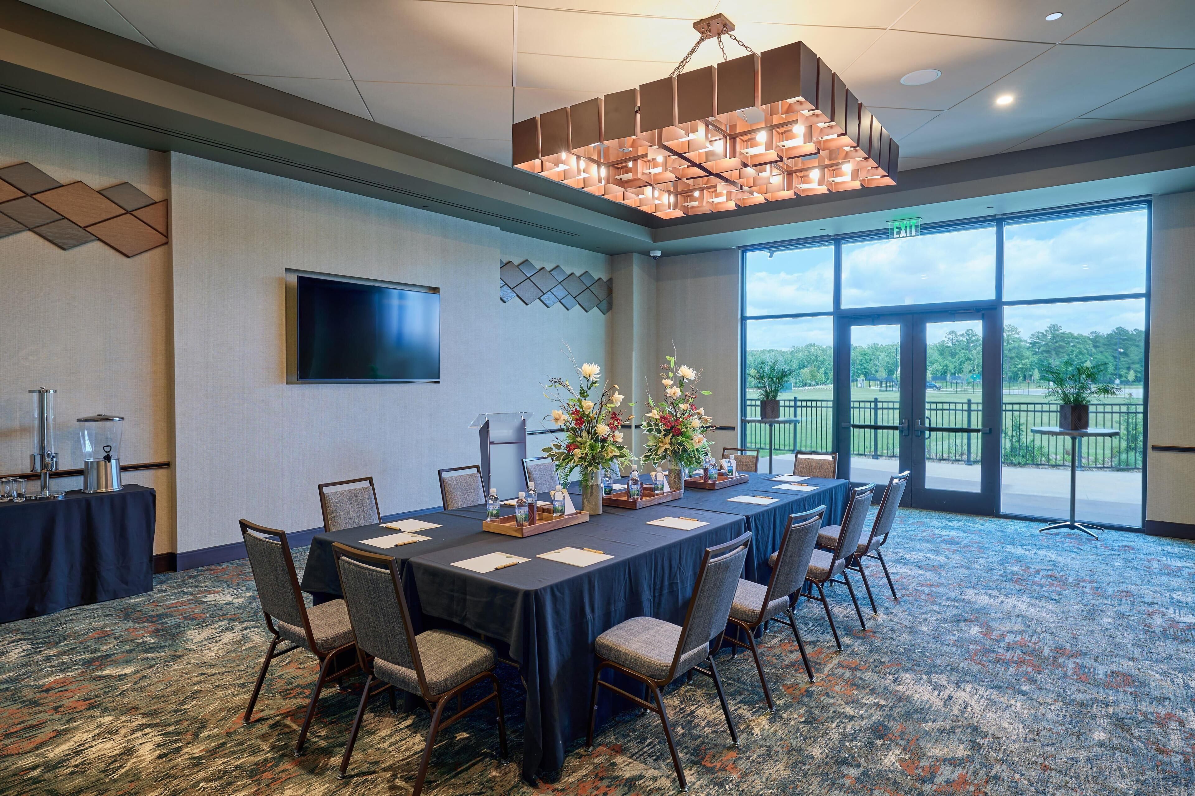 A conference room with a long table, chairs, a flat-screen TV, and a large window with a view.