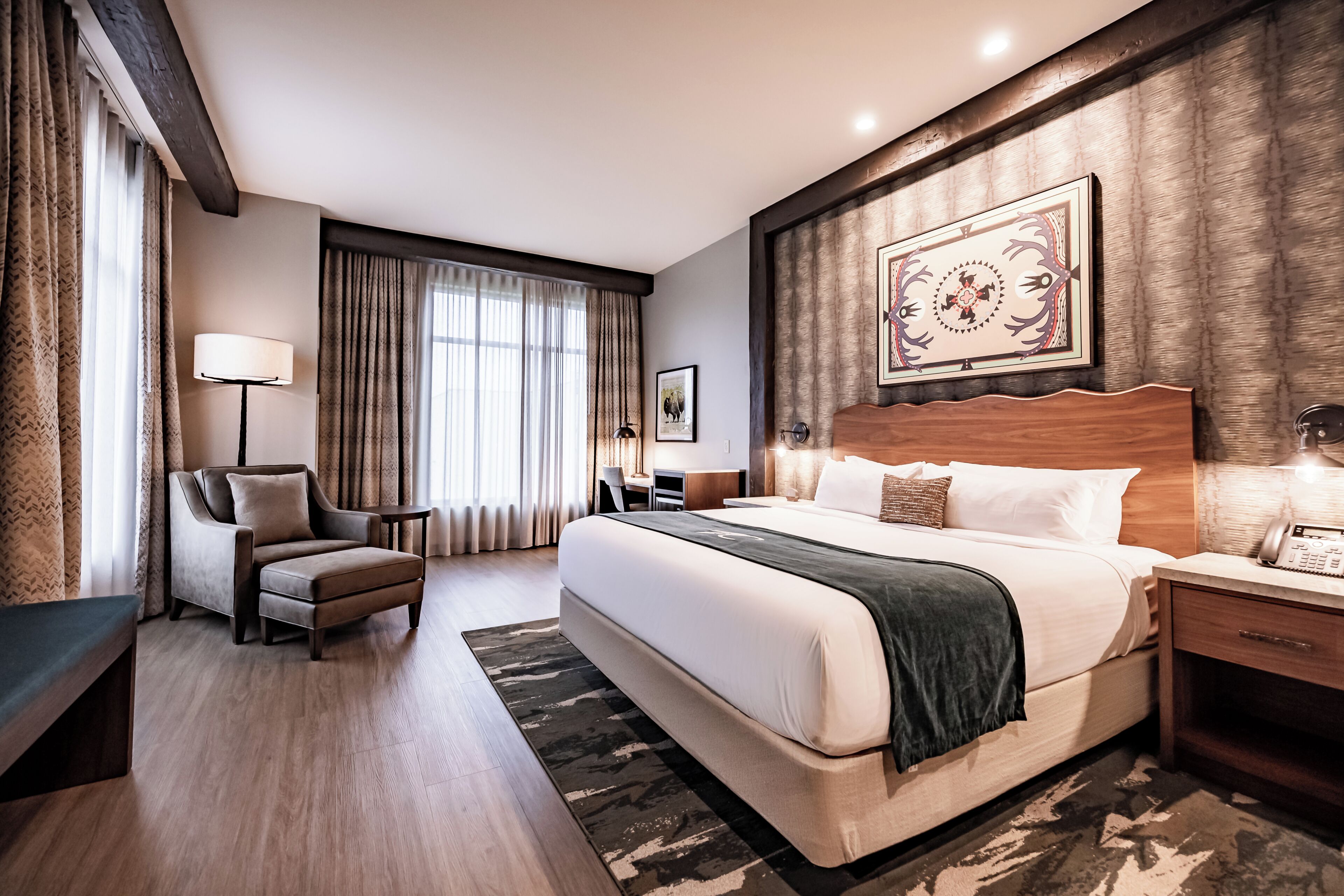 A hotel room with a large bed, a chair, a desk, a lamp, and a painting on the wall.