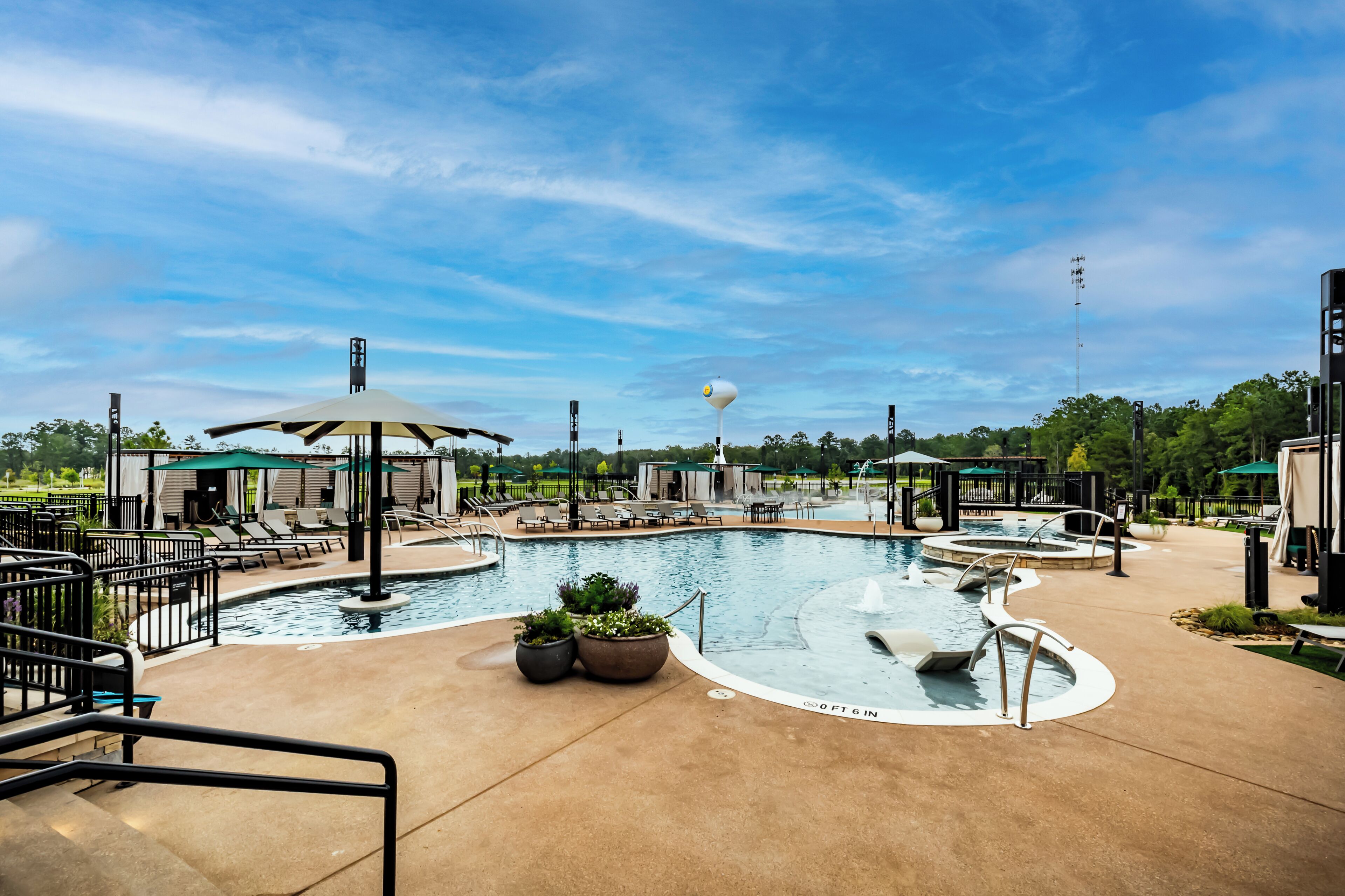A pool area with lounge chairs, umbrellas, and a water feature.